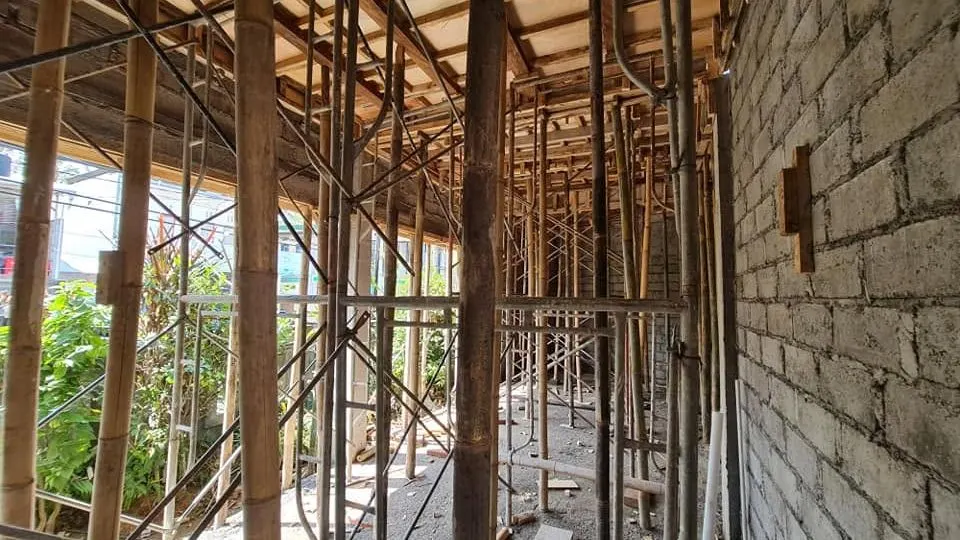 Bamboo and timber shoring under an upper-floor slab with a masonry wall