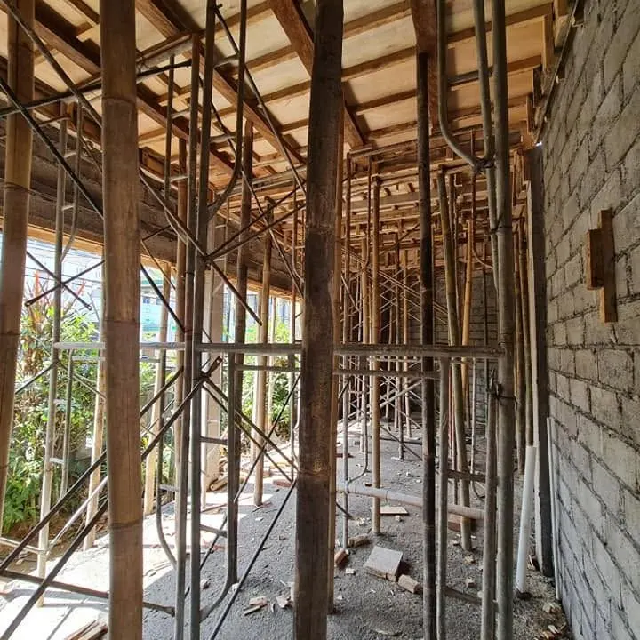 Bamboo and timber shoring under an upper-floor slab with a masonry wall